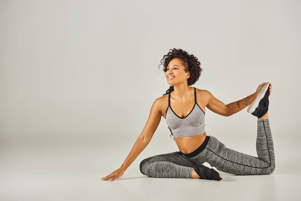 Junge Afroamerikanerin in aktiver Kleidung nimmt anmutig eine Yoga-Pose auf weißem Hintergrund ein. - Foto, Bild