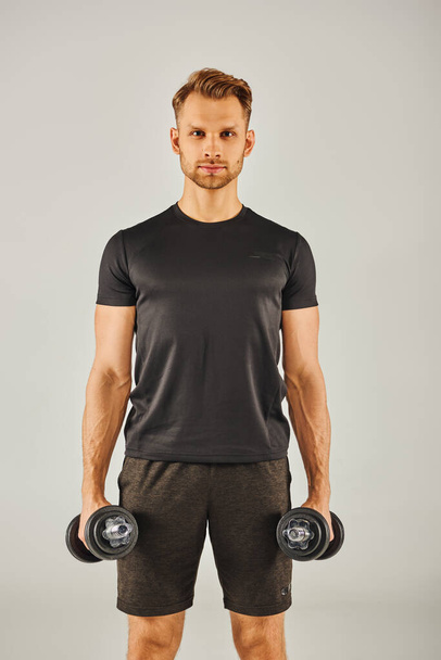 A young sportsman in active wear holding two dumbbells in front of a white background. - Photo, Image