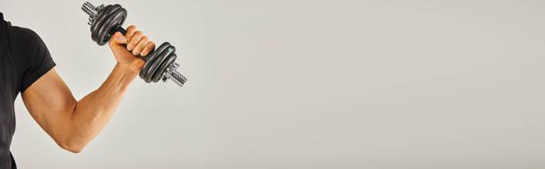 Um jovem desportista em uso ativo está segurando um par de halteres em um estúdio com um fundo cinza, mostrando força e determinação. - Foto, Imagem