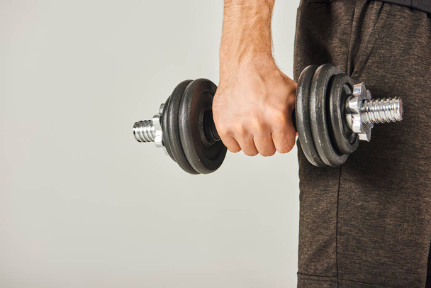 A young sportsman in active wear grips a pair of dumbbells in a studio with a grey background, showcasing strength and determination. - Photo, Image