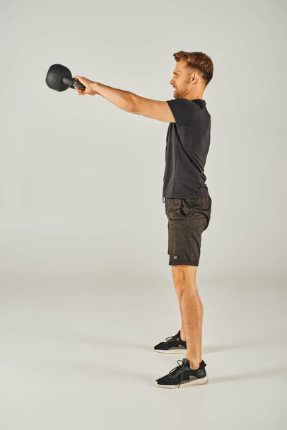 Jonge sporter in actieve kleding showcasing kracht en vastberadenheid met kettlebell op witte achtergrond. - Foto, afbeelding