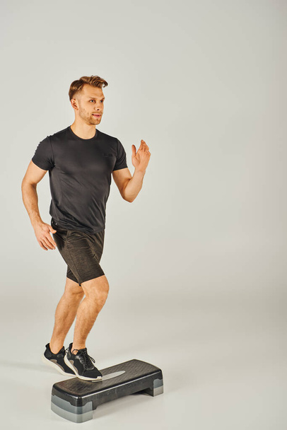 A young sportsman in active wear energetically running on a stepper in a studio against a white background. - Photo, Image