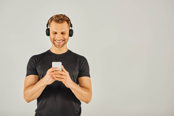 Een jonge man met een koptelefoon staart naar zijn telefoon scherm, geabsorbeerd in zijn digitale wereld. - Foto, afbeelding