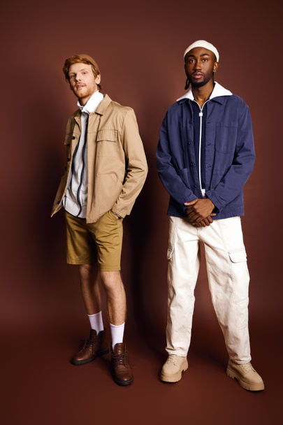 Zwei gutaussehende multikulturelle Männer mit stylischer Kleidung stehen zusammen vor braunem Hintergrund. - Foto, Bild