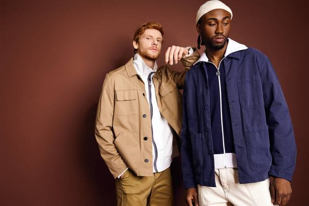 Due uomini multiculturali alla moda in piedi insieme di fronte a un muro marrone. - Foto, immagini