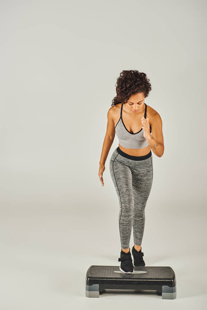 Curly Afro-American sportswoman in active wear stepping up on a white stepper in a studio. - Photo, Image