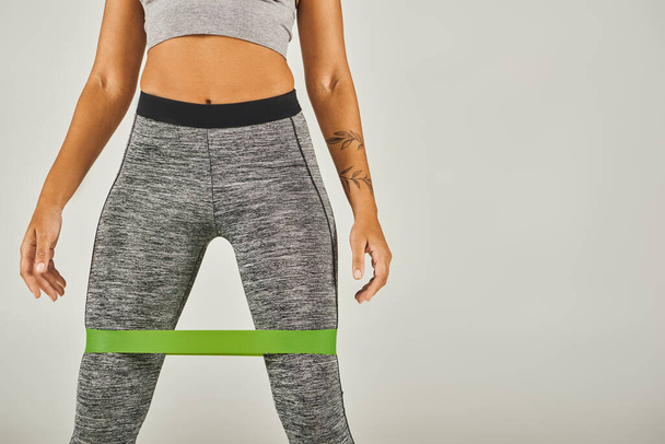 African American sportswoman in green band and leggings, working out in studio with grey background. - Photo, Image