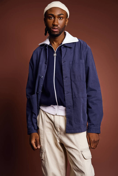 Een knappe jonge Afro-Amerikaanse man in een blauw jasje en bruine broek. - Foto, afbeelding