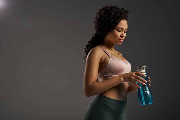 A curly African American sportswoman in a sports bra holding a water bottle, ready for a workout. - Photo, Image