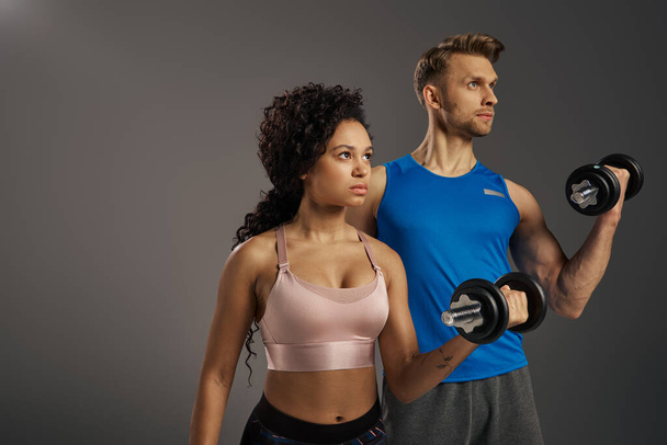 Multicultural man and woman in active wear pose confidently with dumbbells in a studio setting. - Photo, Image