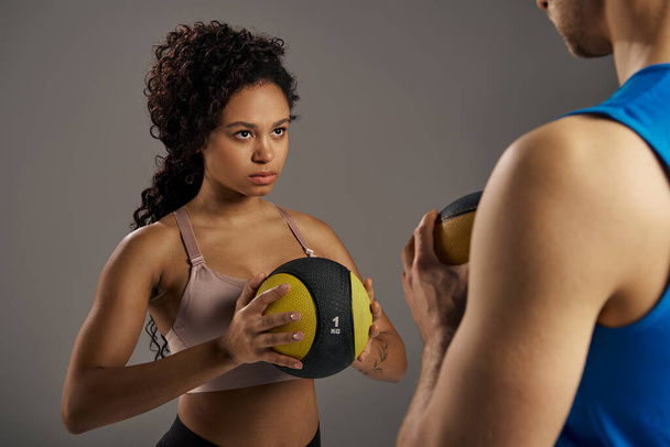A young multicultural and fit couple in active wear holding yellow balls in a studio setting on a grey background. - Photo, Image