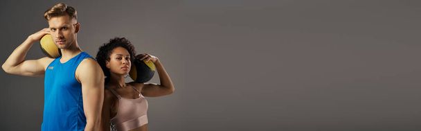Een jong, multicultureel koppel in actieve kleding poseert zelfverzekerd voor de camera tegen een grijze studio achtergrond. - Foto, afbeelding
