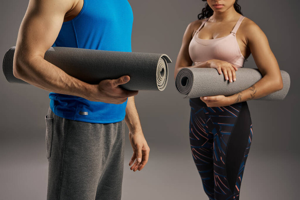 Giovane coppia multiculturale in abbigliamento attivo, in possesso di un tappetino yoga in un ambiente studio su uno sfondo grigio. - Foto, immagini