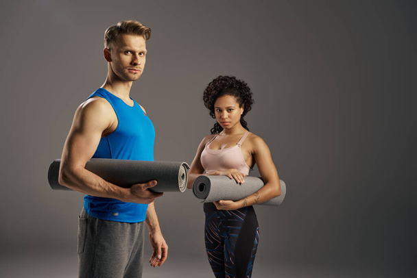 Ein junges multikulturelles und fittes Paar in aktiver Kleidung hält eine Yogamatte in der Hand, bereit für das Workout im Studio. - Foto, Bild
