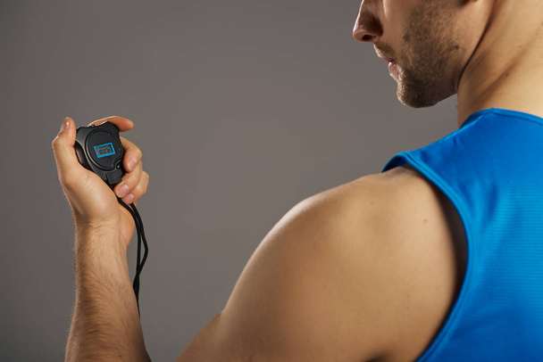 A man in a blue tank top is seen holding an electronic timer. - Photo, Image