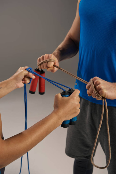 Un homme et une femme, jeunes et multiculturelles, en tenue active, tiennent des cordes de saut dans un studio de fitness sur fond gris. - Photo, image