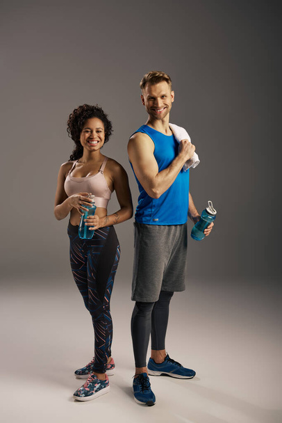 Un jeune couple multiculturel en tenue active, en pleine forme, posant en toute confiance dans un studio sur fond gris. - Photo, image
