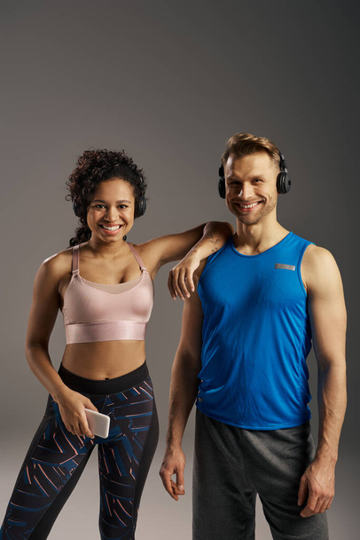 A fit multicultural couple in activewear strikes a pose together in a studio against a grey background. - Photo, Image
