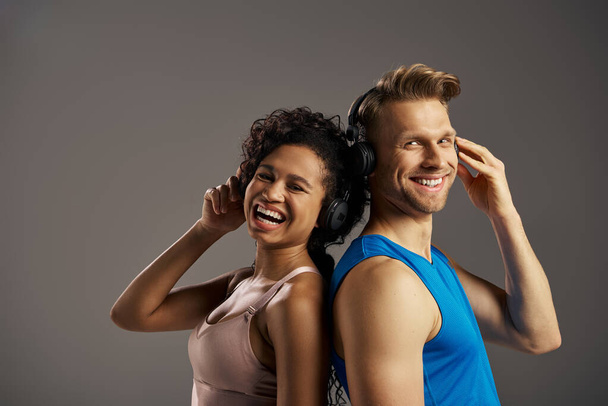 Ένας νεαρός άνδρας και μια γυναίκα σε activewear βυθίζονται στη μουσική, ακούγοντας μέσα από ακουστικά με εκφράσεις χαράς και σύνδεσης. - Φωτογραφία, εικόνα