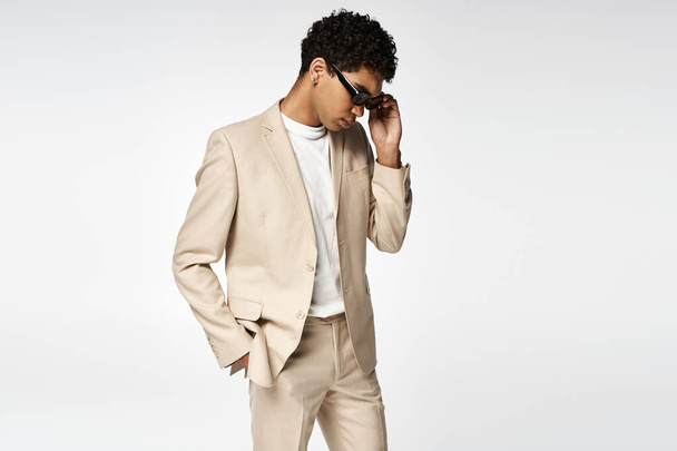 Knappe Afro-Amerikaanse man in beige pak en stijlvolle zonnebril. - Foto, afbeelding