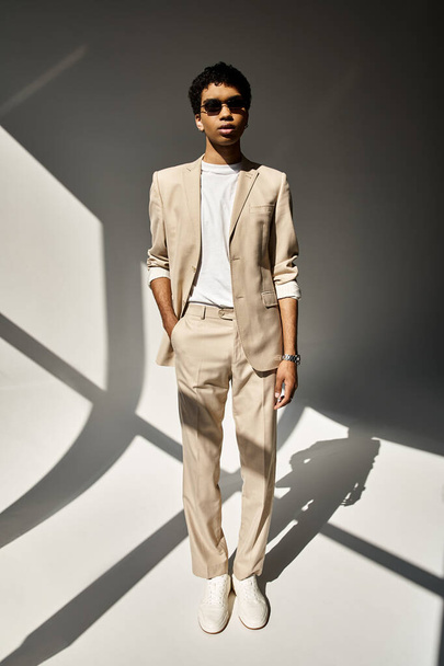Knappe Afro-Amerikaanse man in beige pak en stijlvolle zonnebril voor de witte muur. - Foto, afbeelding