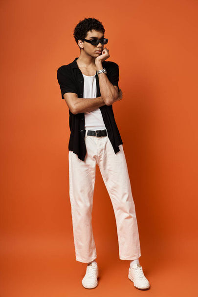 Симпатичный афроамериканец в белых брюках и черной рубашке, позирует перед оранжевым фоном.. - Фото, изображение