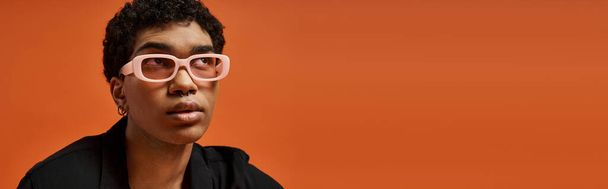 Hombre afroamericano guapo en gafas de color rosa contra fondo naranja. - Foto, Imagen
