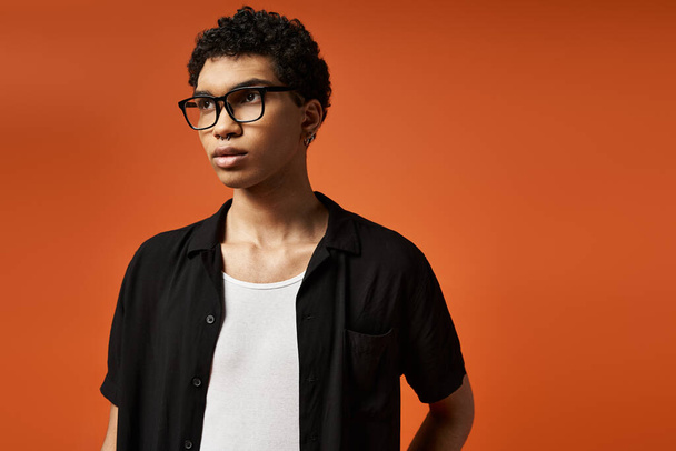 Knappe Afro-Amerikaanse man met een stijlvolle bril staat vol vertrouwen tegen een levendige oranje achtergrond. - Foto, afbeelding