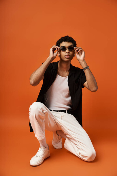Handsome man in white pants and sunglasses crouching on orange background. - Photo, Image
