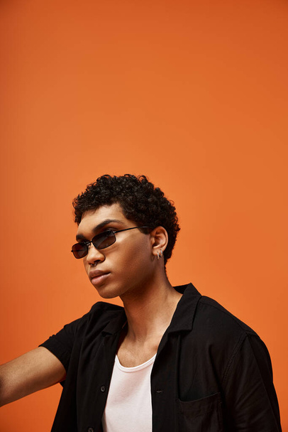 Schöner junger Mann mit Sonnenbrille vor leuchtend orangefarbener Kulisse. - Foto, Bild