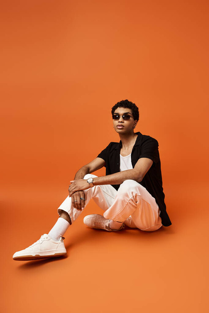 Стильный афроамериканец сидит на ярко-оранжевом фоне в белых кроссовках. - Фото, изображение