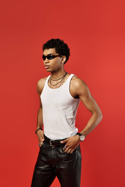 Jóképű afro-amerikai férfi elegáns napszemüvegben, fehér felsőben és bőrnadrágban. - Fotó, kép