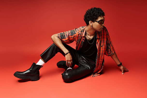 A stylish African American man in a red shirt and leather pants sits on the floor. - Photo, Image