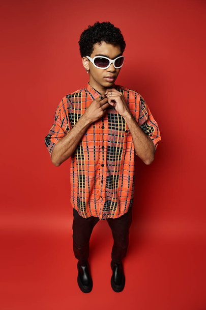 Handsome African American man in orange shirt and sunglasses striking a pose on red backdrop. - Photo, Image