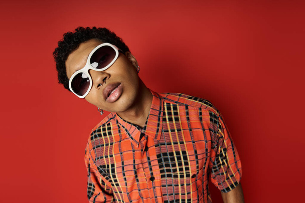 Handsome African American man in plaid shirt and sunglasses on vibrant red background. - Photo, Image