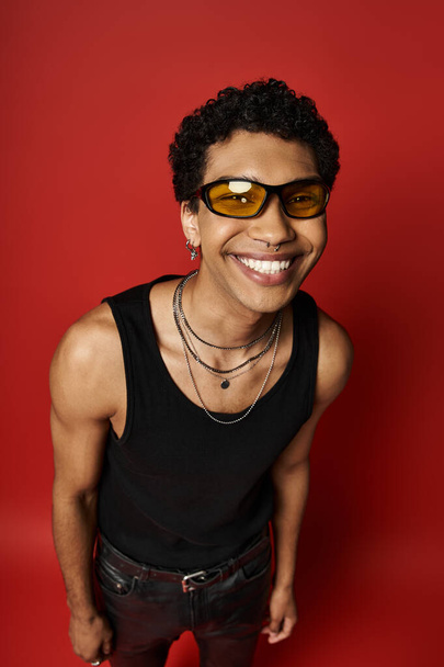 Egy mosolygós afro-amerikai férfi elegáns napszemüveget visel élénk vörös háttérrel.. - Fotó, kép