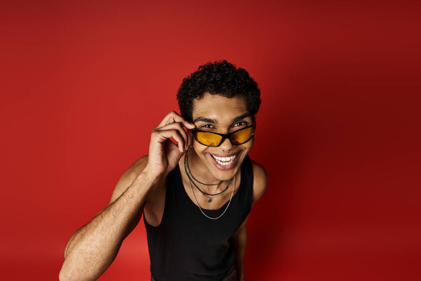 Ein gutaussehender afroamerikanischer Mann trägt selbstbewusst eine Sonnenbrille auf einem fetten roten Hintergrund. - Foto, Bild