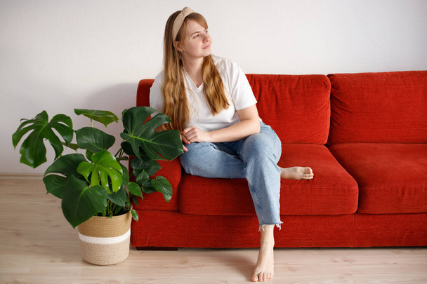 ελκυστική γυναίκα τριαντάρα κάθεται στον καναπέ στο σπίτι και κοιτάζει αλλού - Φωτογραφία, εικόνα