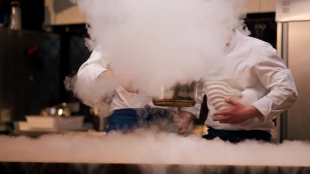 deux chefs en uniformes blancs préparent de l'azote liquide dans la cuisine qui se répand sur toute la table coup - Séquence, vidéo