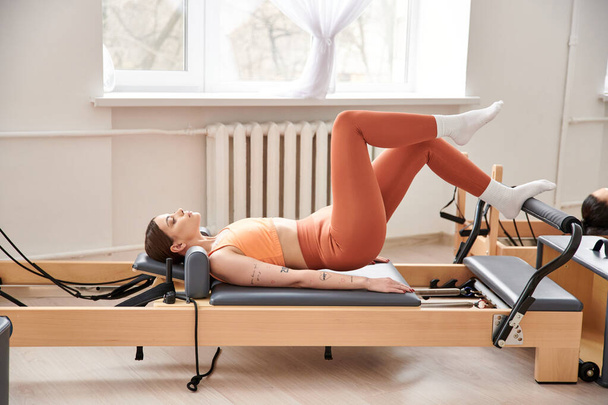 Een sportieve vrouw in een oranje top houdt zich bezig met een pilates routine. - Foto, afbeelding