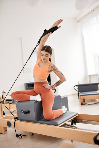 Eine sportliche Frau in orangefarbenem Oberteil und Hose während einer Pilates-Stunde. - Foto, Bild