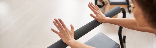 Μια αθλητική γυναίκα απλώνει χαριτωμένα τα χέρια της σε ένα μπαρ κατά τη διάρκεια ενός μαθήματος πιλάτες. - Φωτογραφία, εικόνα