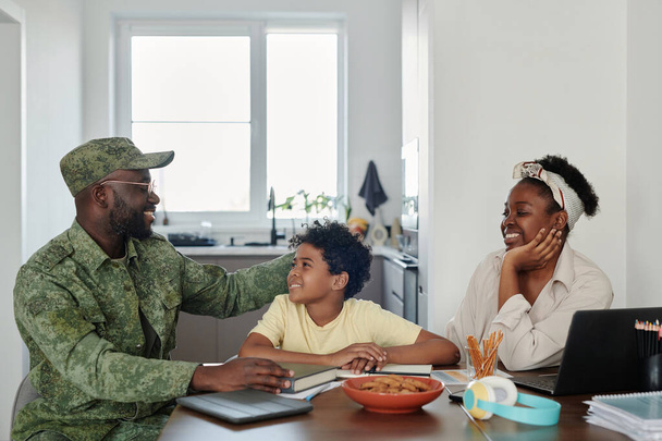 Familie blij om te zien dat hun vader terugkeert uit de oorlog, ze zitten aan tafel in de keuken en praten met elkaar - Foto, afbeelding