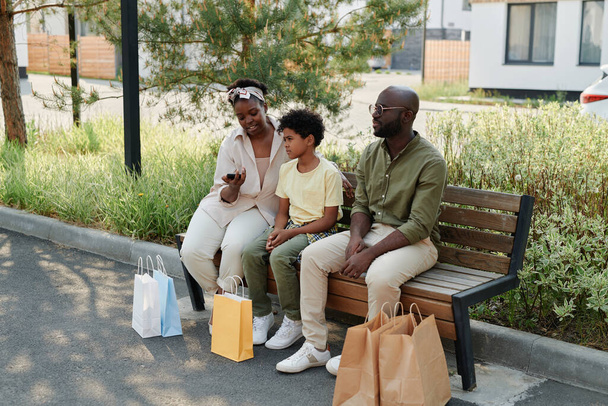 Afrikai amerikai család pihen a szabadban a padon bevásárló táskák vásárlás után - Fotó, kép