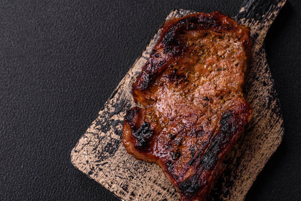 Ízletes szaftos marhahús a csonton, tomahawk sóval, fűszerekkel és fűszernövényekkel sötét beton alapon - Fotó, kép