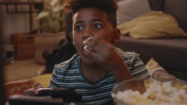 Aufnahmen von afroamerikanischen Kindern mit weit aufgerissenen Augen, die aufgeregt auf den Fernsehbildschirm starren, während sie Konsolen-Videospiel spielen und in den 90er Jahren zu Hause Popcorn verschlingen - Filmmaterial, Video