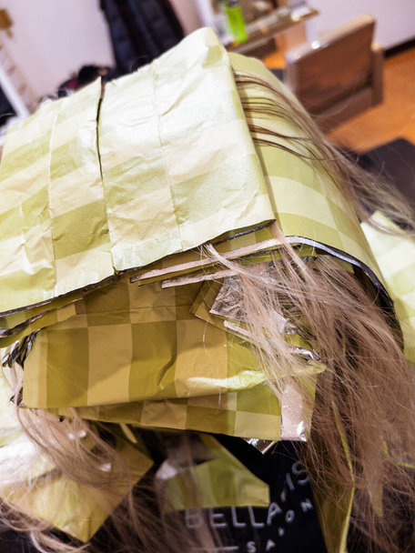 Les mèches de cheveux jettent un coup d'oeil à travers une série de feuilles jaunes méticuleusement disposées pour un traitement de mise en évidence. L'ambiance des salons se reflète en arrière-plan, où les stylistes concentrés exécutent leur métier - Photo, image