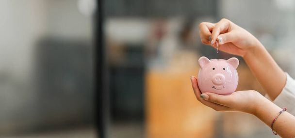 Manos insertando una moneda en una alcancía rosa, simbolizando el concepto de ahorro y responsabilidad financiera - Foto, imagen