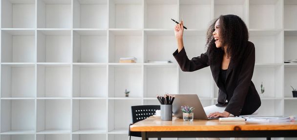 Mujer de negocios alegre levanta la mano en la emoción mientras trabaja en su computadora portátil en su escritorio de la oficina, celebrando un momento exitoso. - Foto, Imagen