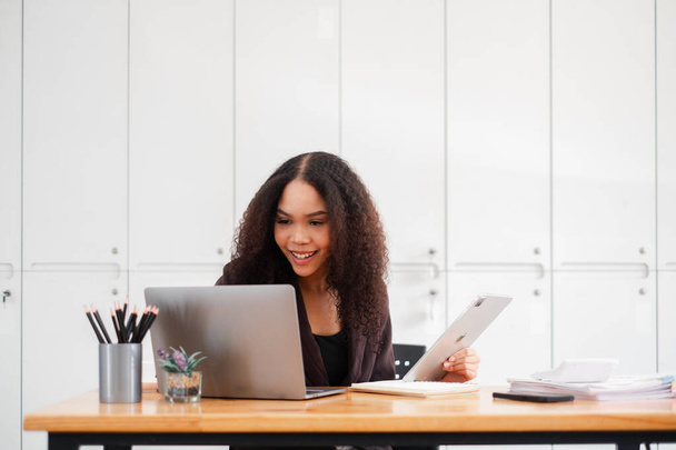 Allegro business woman multitasking, lavorando con un computer portatile e tablet alla scrivania del suo ufficio, trasudando un senso di soddisfazione e produttività. - Foto, immagini